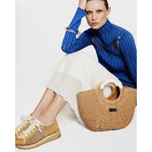 Load image into Gallery viewer, Woman in blue sweater and white skirt sitting with a straw bag on a white background
