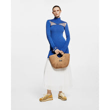 Load image into Gallery viewer, Person wearing a blue ribbed sweater and white skirt, holding a woven bag on a light gray background
